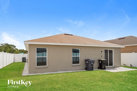 a small brown house with a grass yard and a white fence