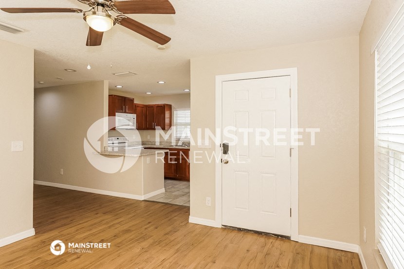 a living room and kitchen with a white door and a ceiling fan