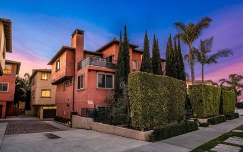 A house with a red facade is surrounded by greenery and trees.