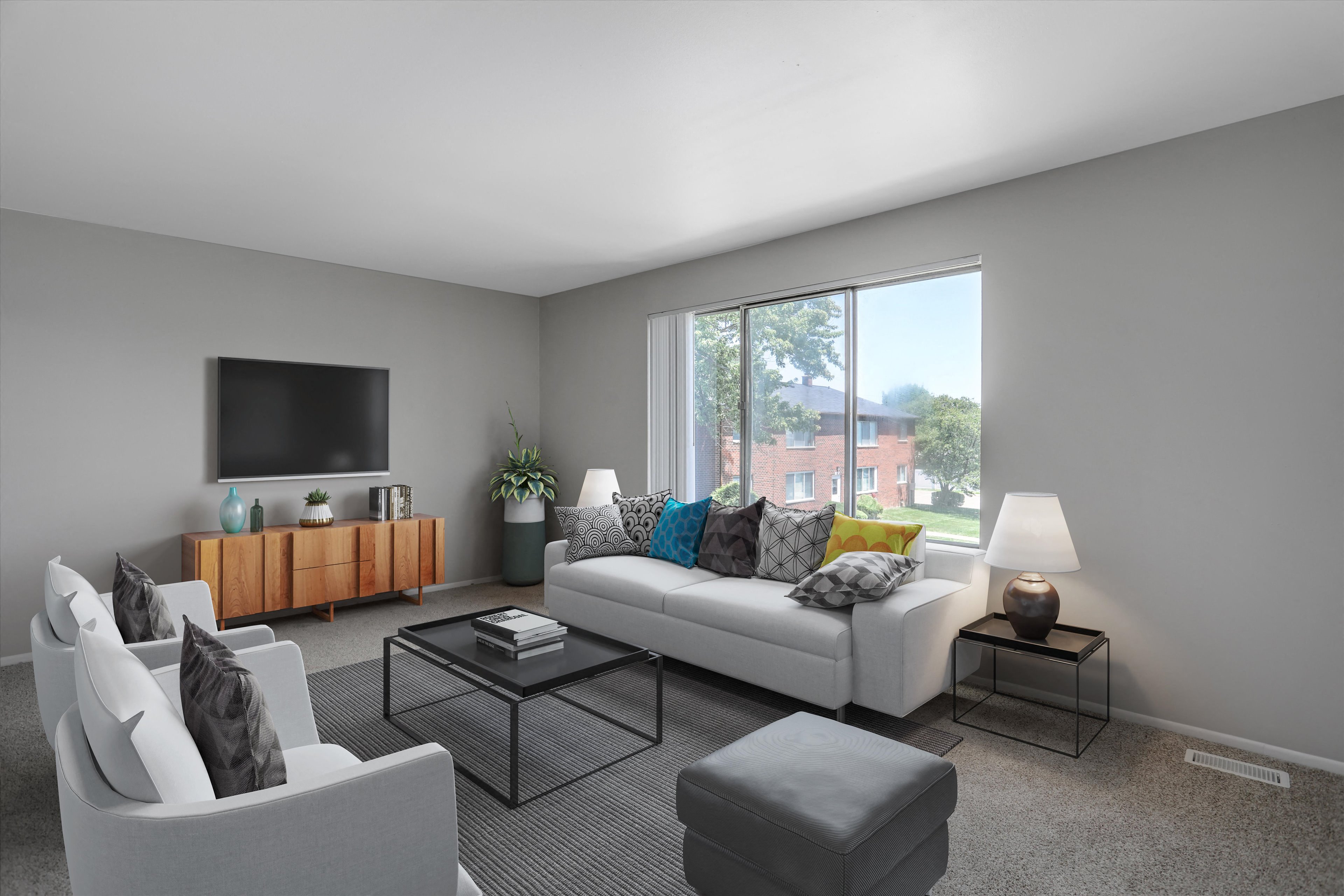 A living room with a white couch, a grey armchair, a glass coffee table, and a television on the wall.