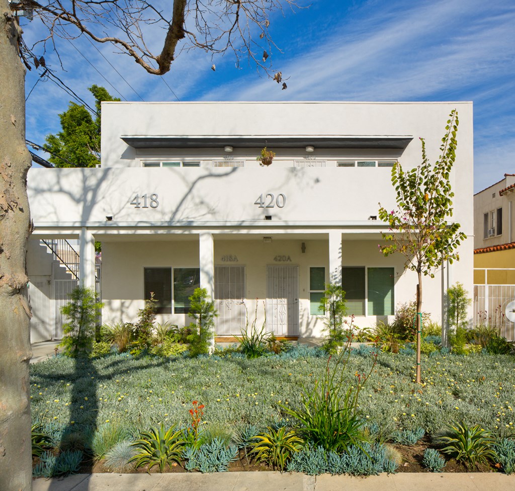 the front of a white building with plants in front of it