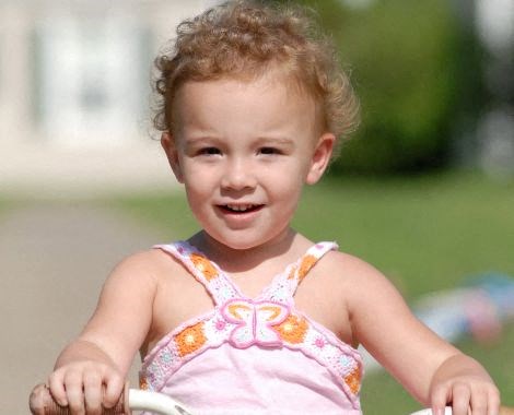 a little girl in a pink dress riding a bike