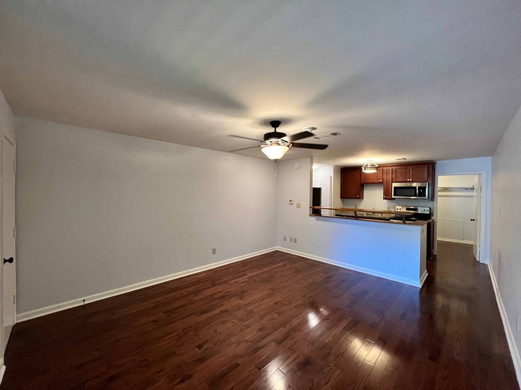 an empty living room and kitchen with wood floors and a ceiling fan