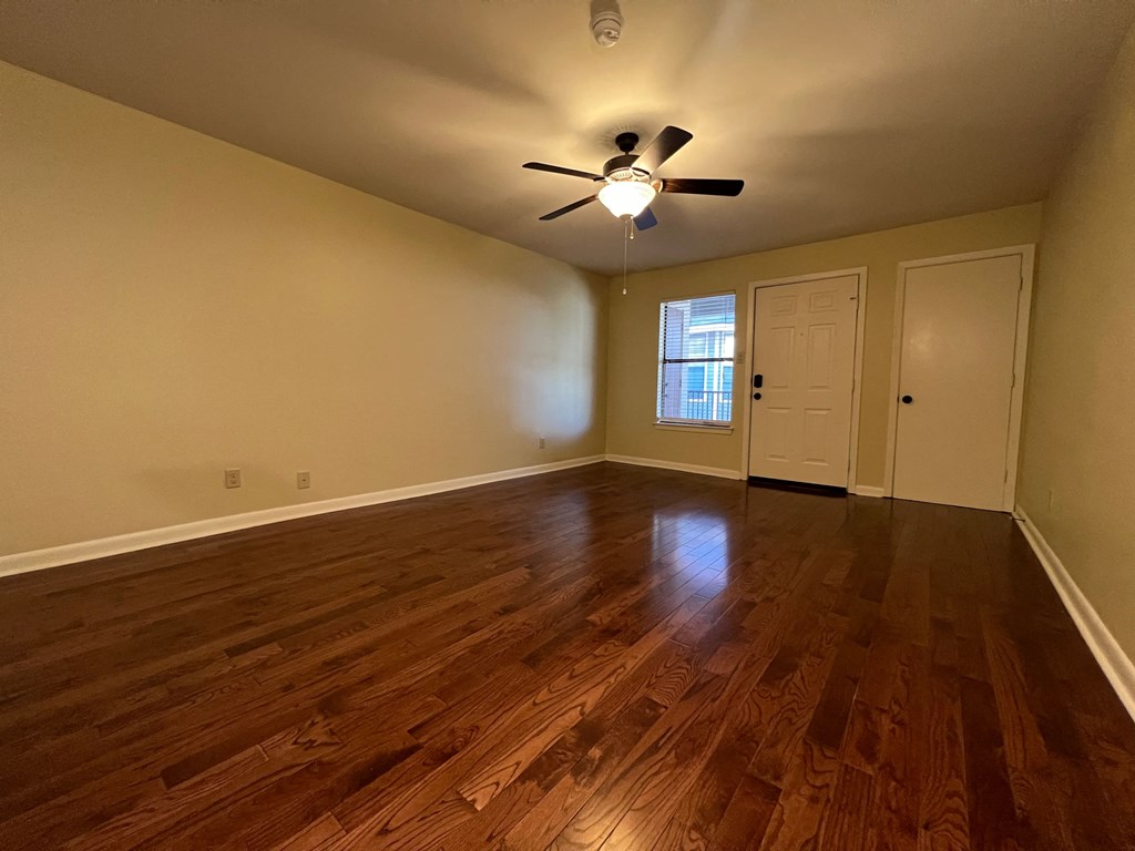 an empty living room with wood floors and a ceiling fan