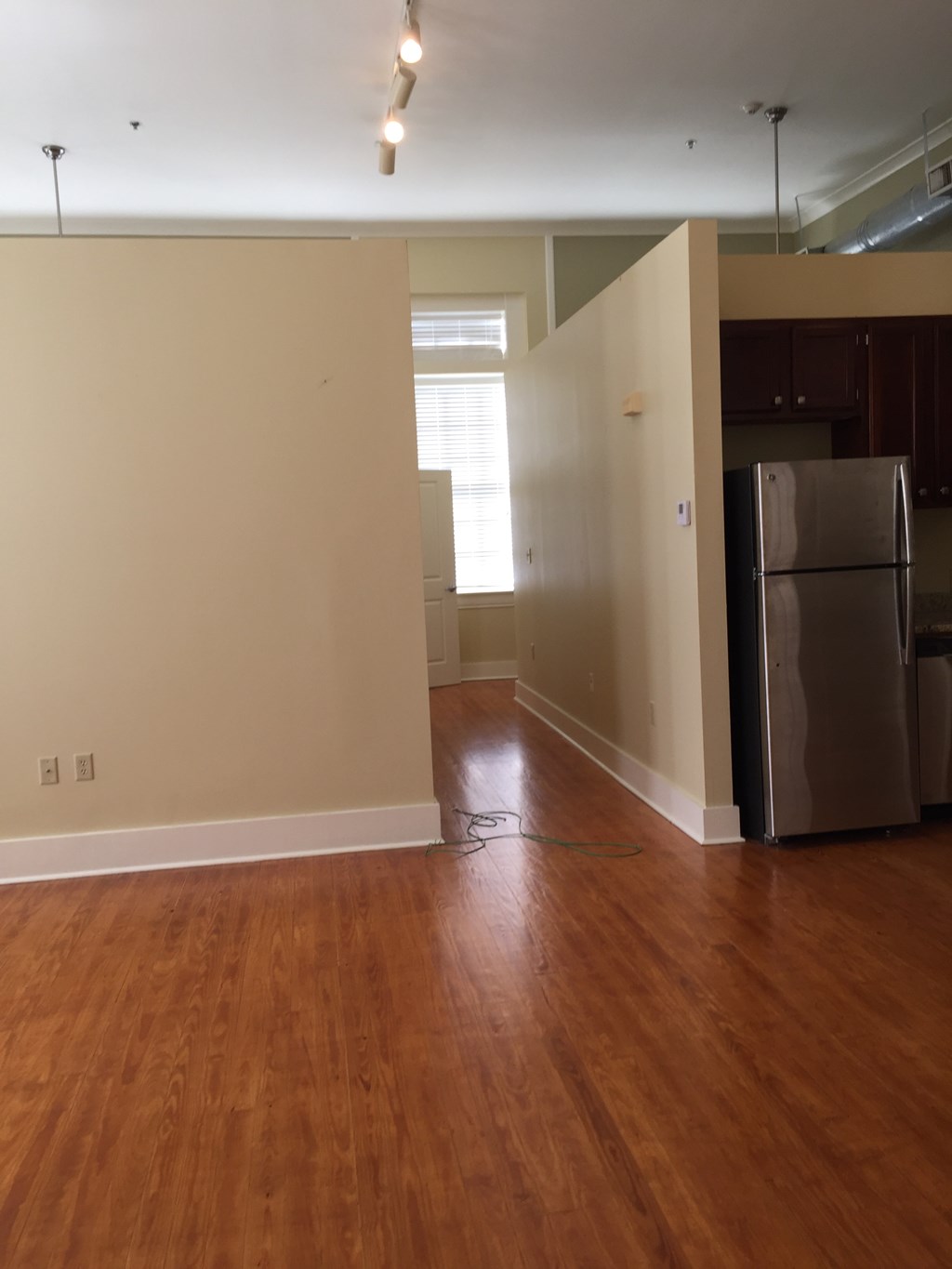 an empty living room with a refrigerator and wood floors