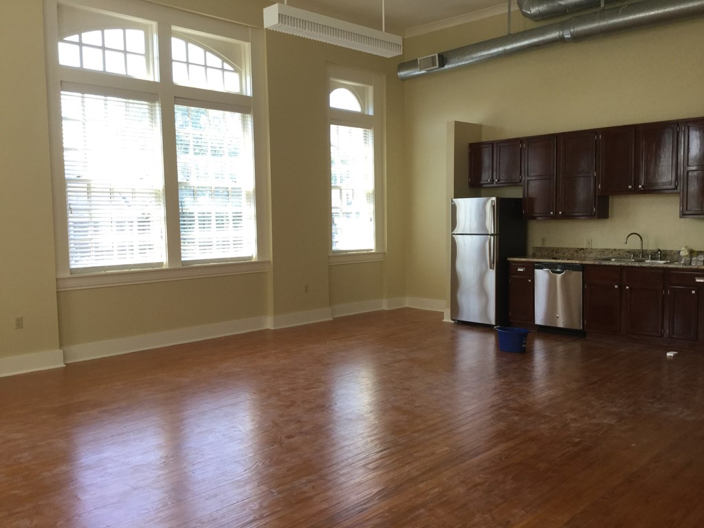 an empty kitchen and living room with wood floors and a stainless steel refrigerator