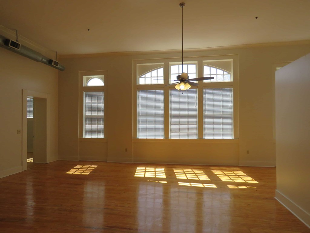 an empty living room with large windows and a ceiling fan