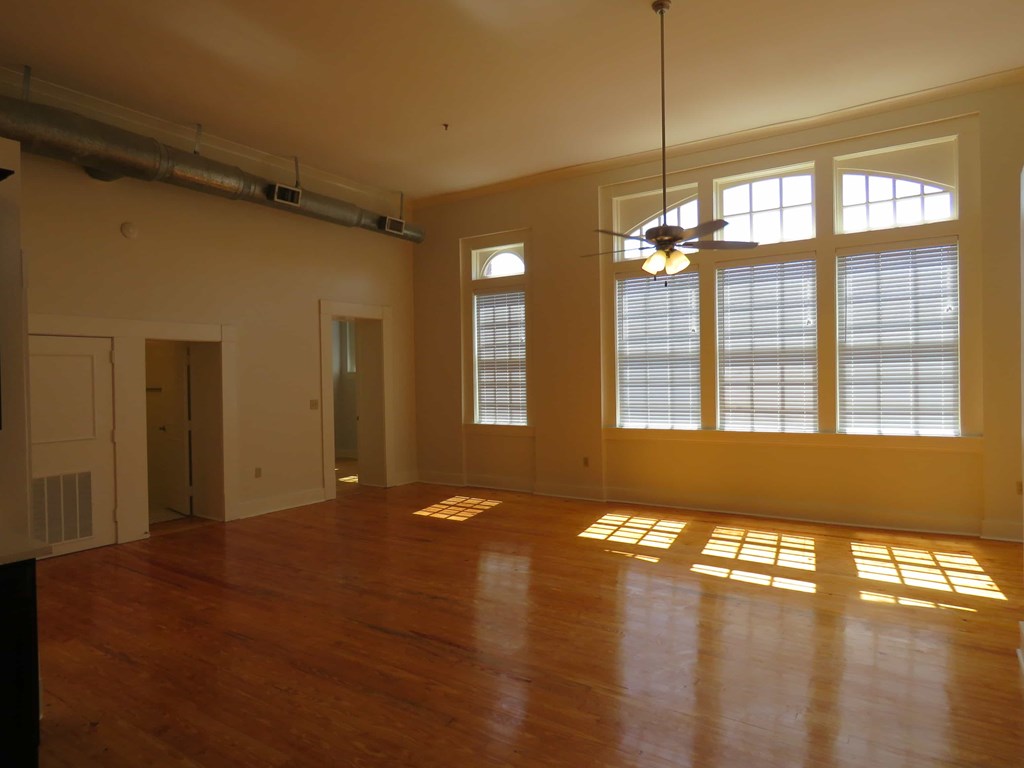 an empty living room with a ceiling fan and large windows