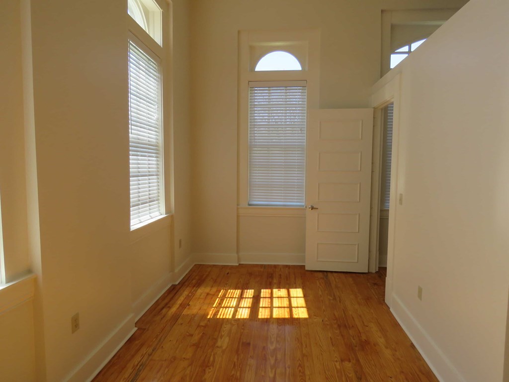 a sunlit room with a door and window and a wooden floor