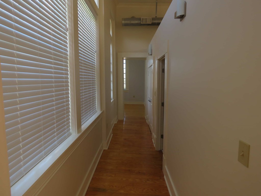 a hallway with white shuttered windows and a wood floor