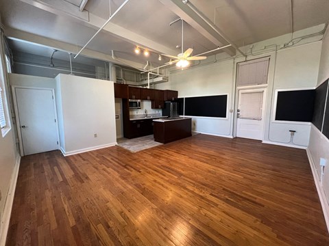 an empty living room with wood floors and a kitchen