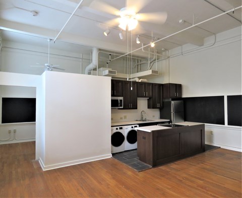 a kitchen with a washer and dryer and black cabinets and a white wall