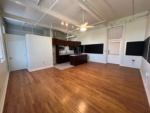 an empty living room with wood floors and a kitchen