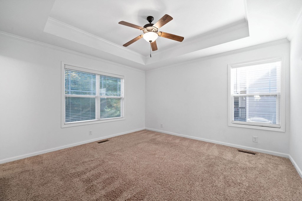 an empty living room with a ceiling fan and two windows