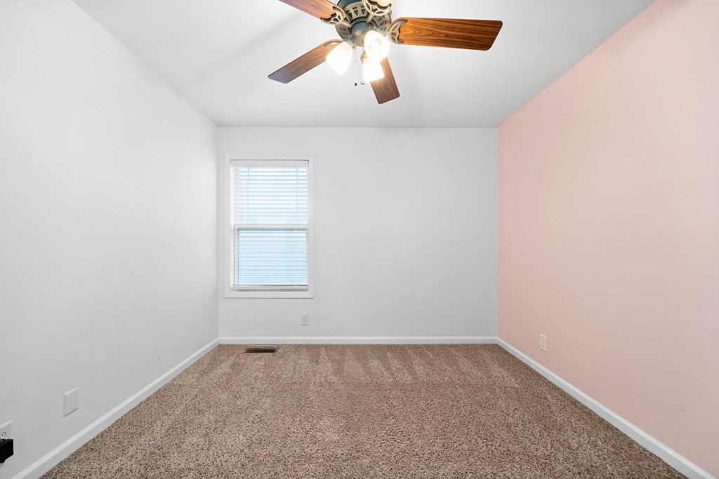 an empty bedroom with a ceiling fan and carpet