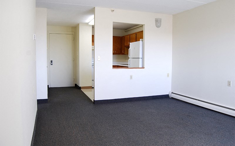 an empty living room with white walls and a white refrigerator