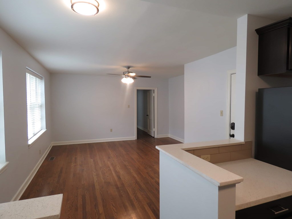 an empty living room and kitchen with wood floors and a ceiling fan