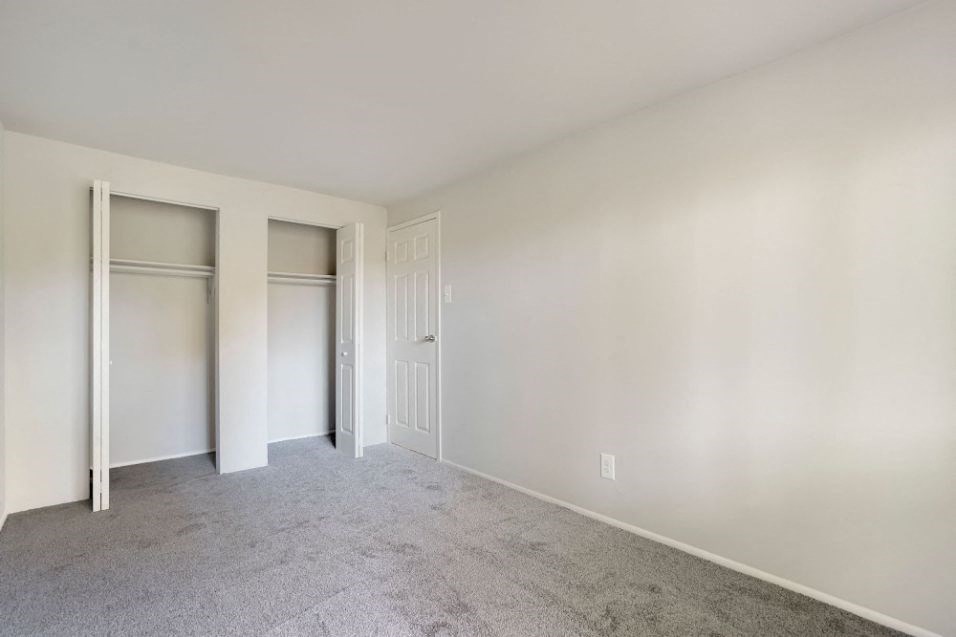 an empty bedroom with white walls and doors to closets