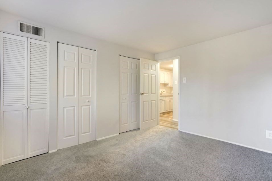 an empty bedroom with white closets and a carpeted floor