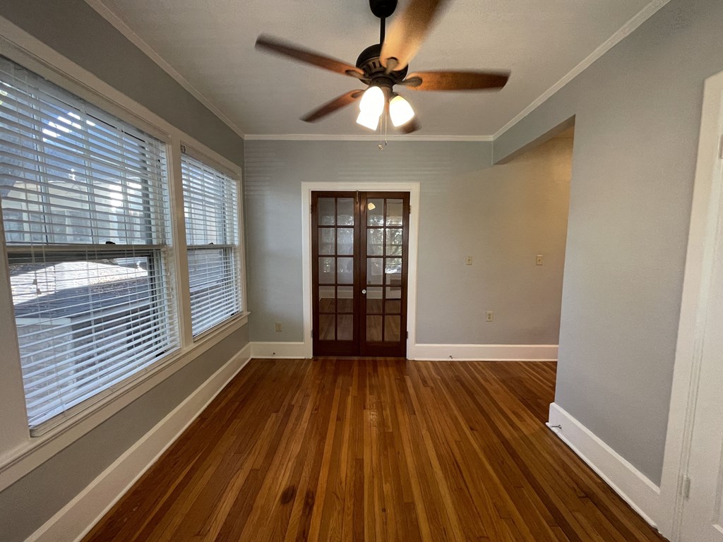 an empty living room with a ceiling fan and large windows