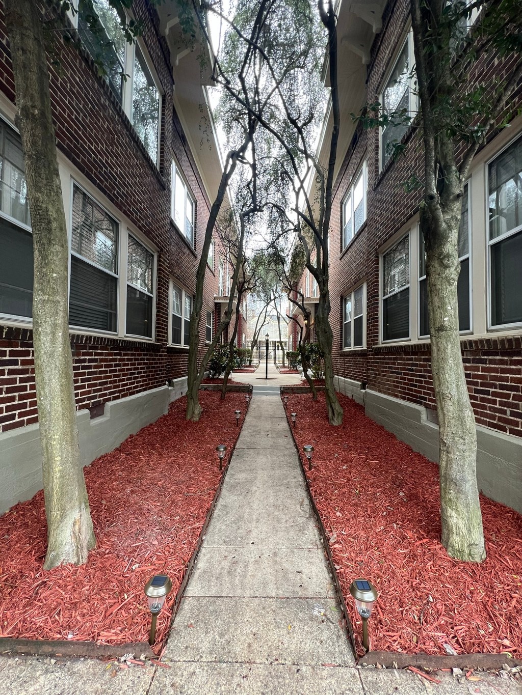 a sidewalk with red mulch in front of a brick building