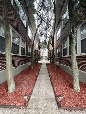 an empty sidewalk in front of a brick building with trees