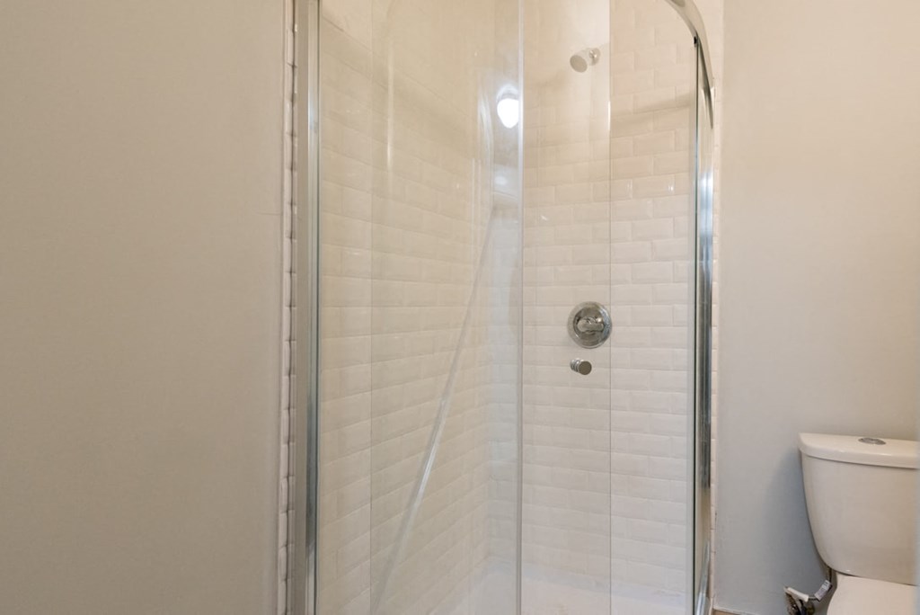 A white toilet sits next to a white tiled shower.