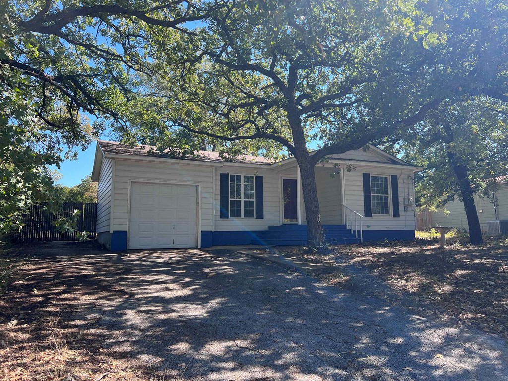 A small white house with a blue trim is surrounded by trees.