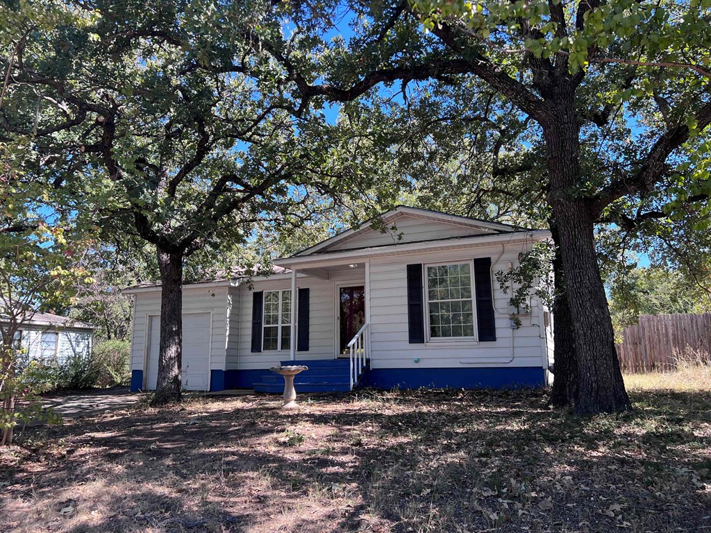A small white house with a blue trim is surrounded by trees.