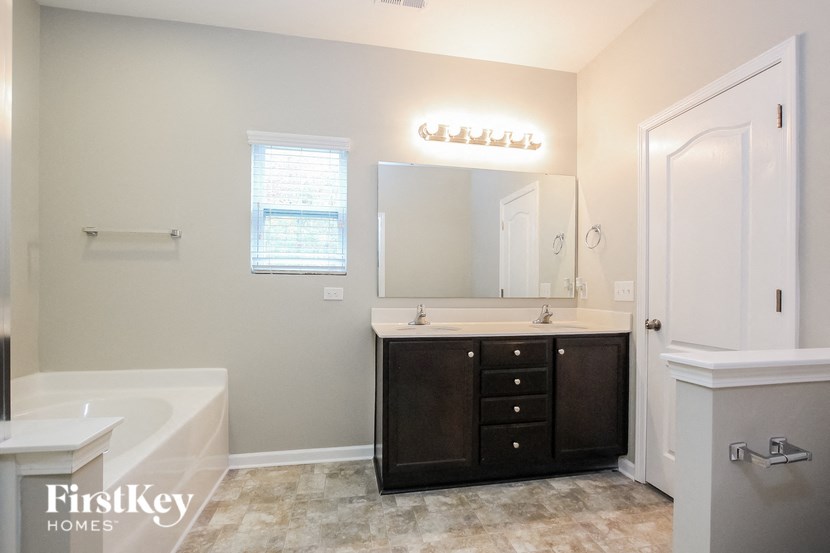 A bathroom with a white tub, sink, and a mirror with lights above it.