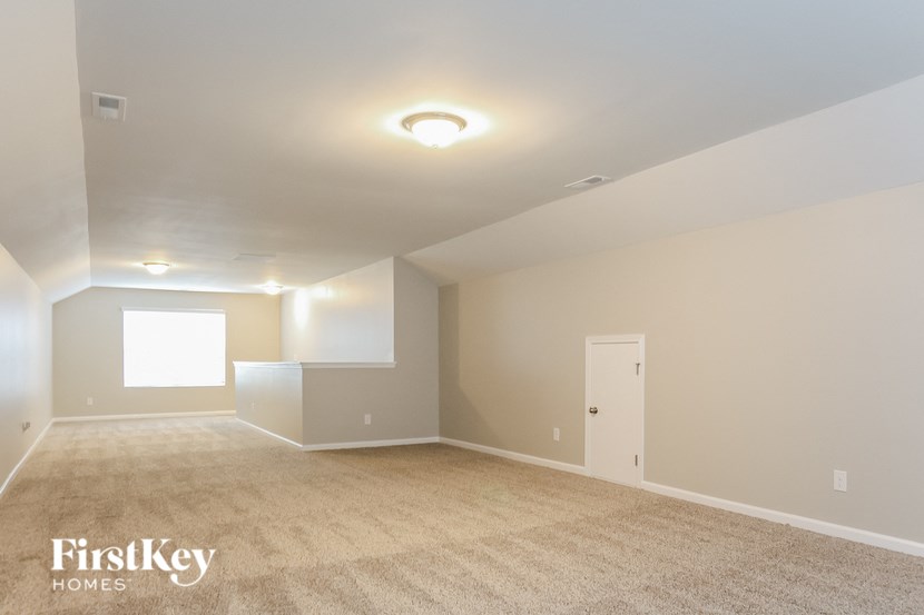 A spacious empty room with a carpeted floor and a door on the right side.