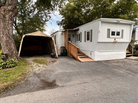 A white RV is parked in a driveway with a brown canopy over it.