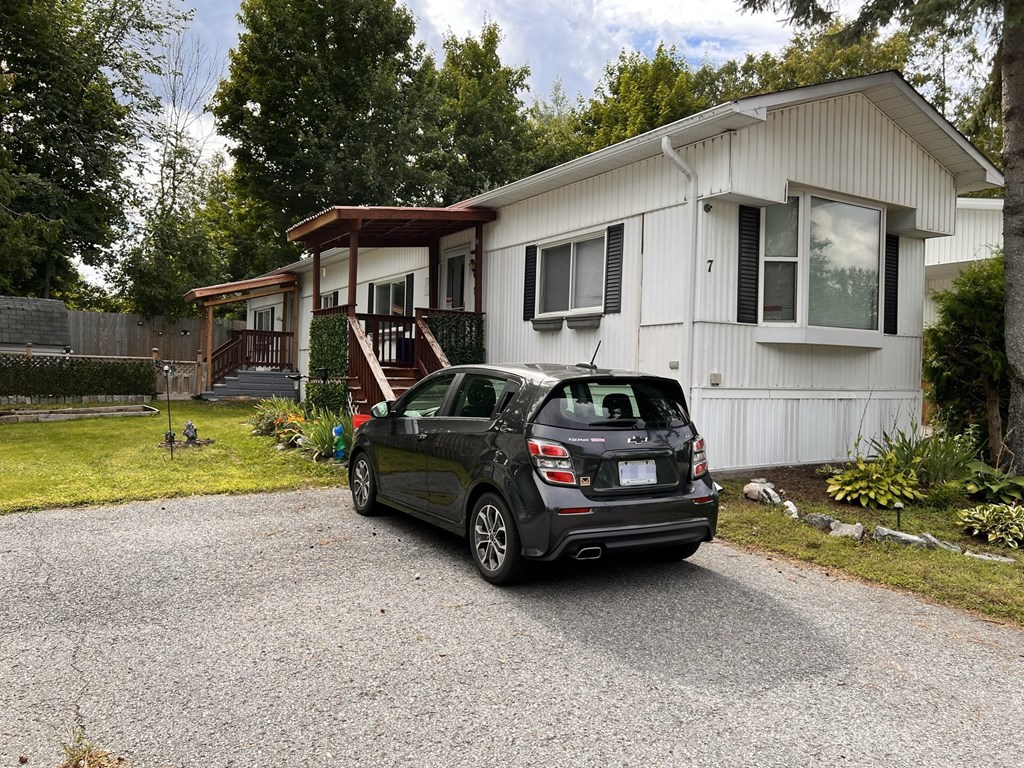 A car is parked in front of a white house with a brown roof.