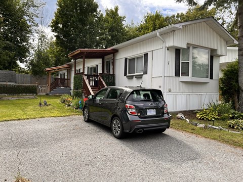 A car is parked in front of a white house with a brown roof.