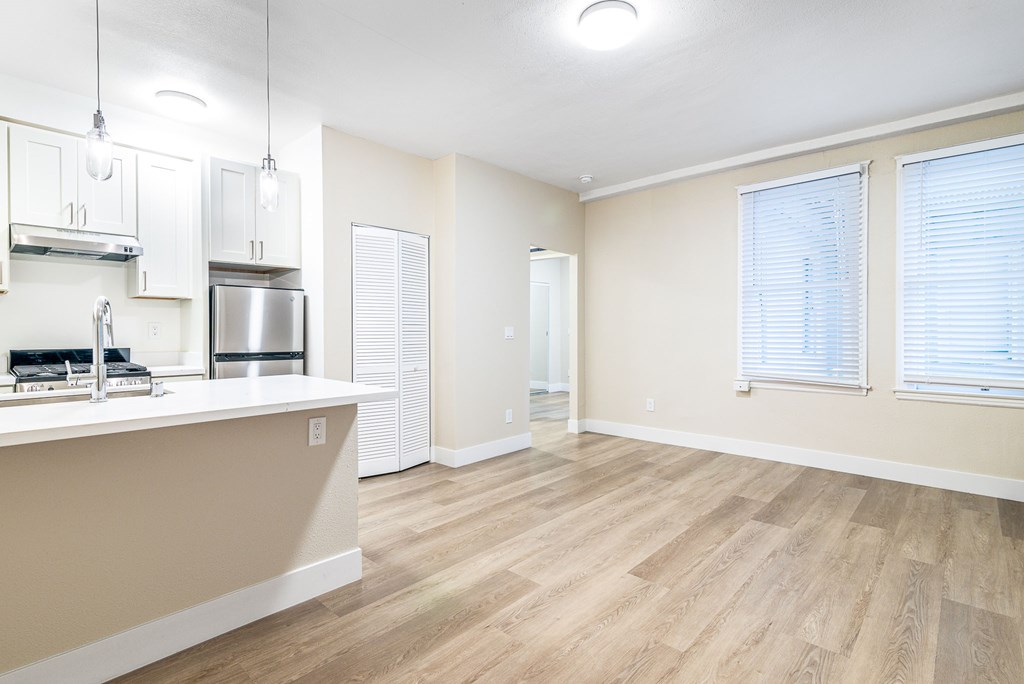 an empty living room and kitchen with wood flooring and white walls