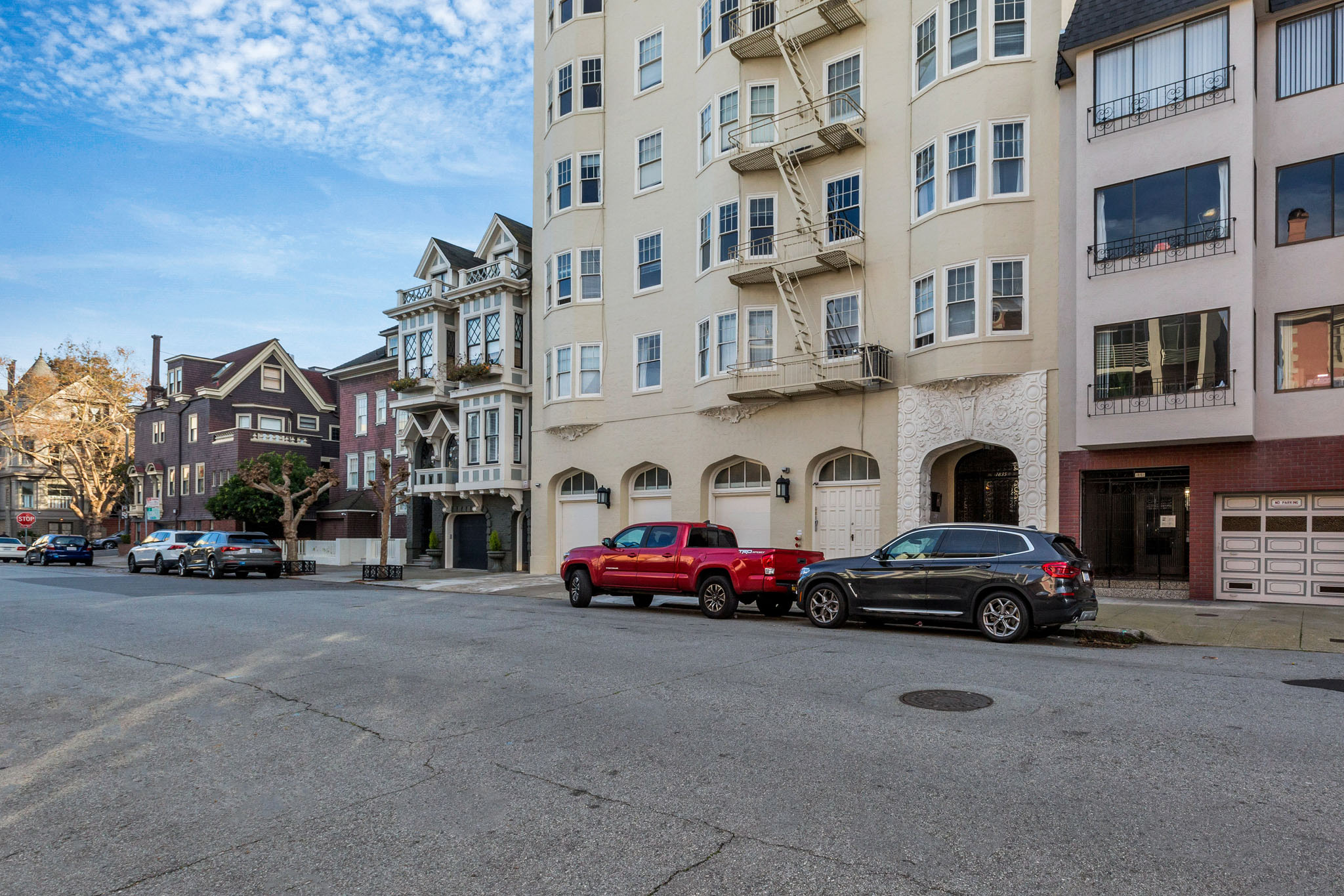 A red car is parked on the street in front of a white building.