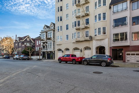 A red car is parked on the street in front of a white building.