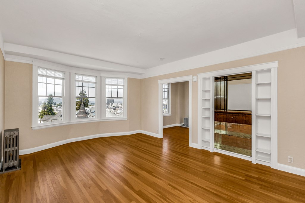 an empty living room with hard wood floors and a window with a mirrored door