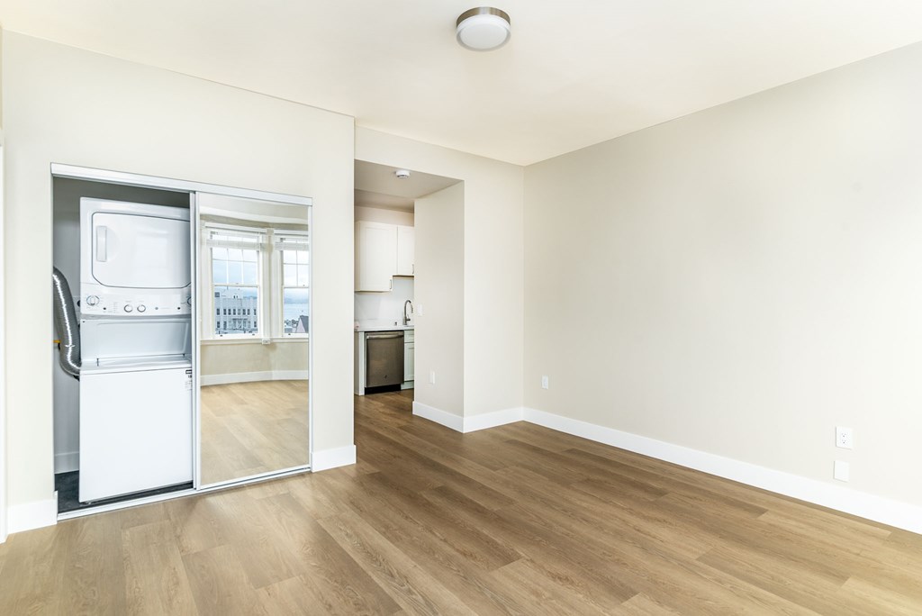an empty living room with wood floors and a kitchen