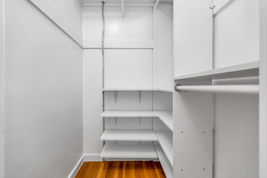 a walk in closet with white walls and shelves and a wood floor