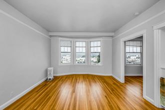 an empty living room with wood floors and three windows