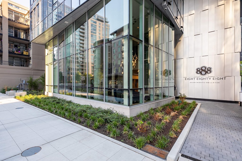 the facade of a building with large glass windows and a sidewalk with plants