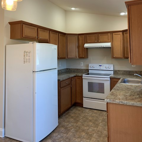 A white refrigerator stands in a kitchen with brown cabinets.
