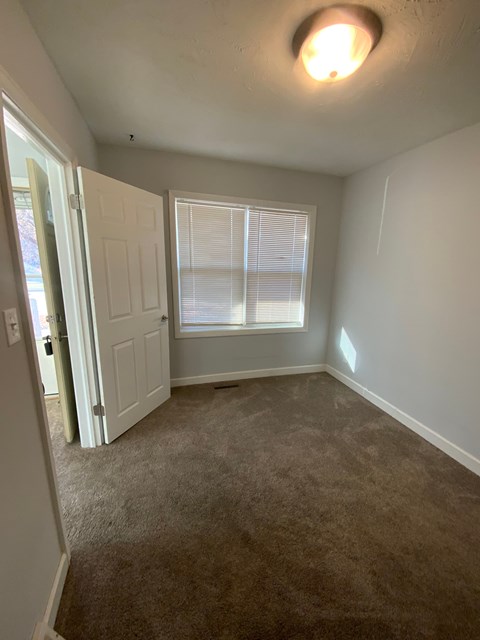 A room with a carpeted floor and a window with blinds.