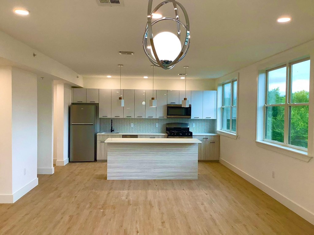 an empty kitchen with a large island and a stainless steel refrigerator