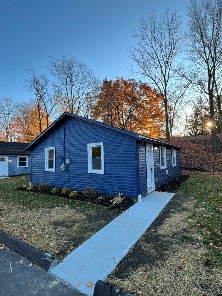 A blue house with a white door and windows is surrounded by trees.