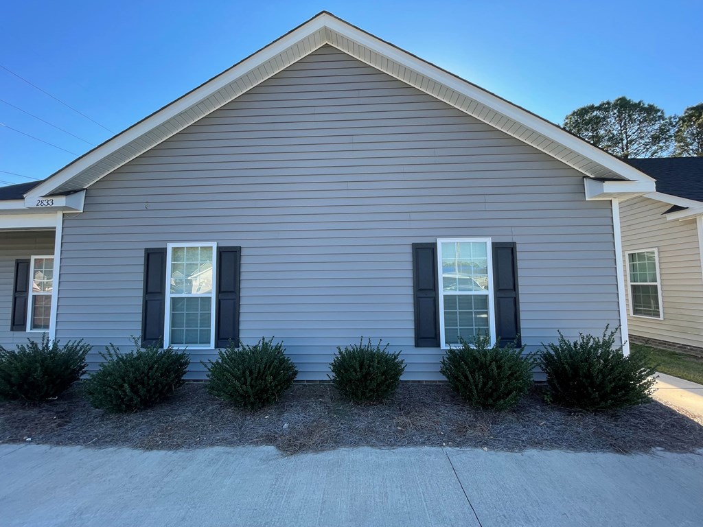 A house with a grey siding and two windows with black shutters.