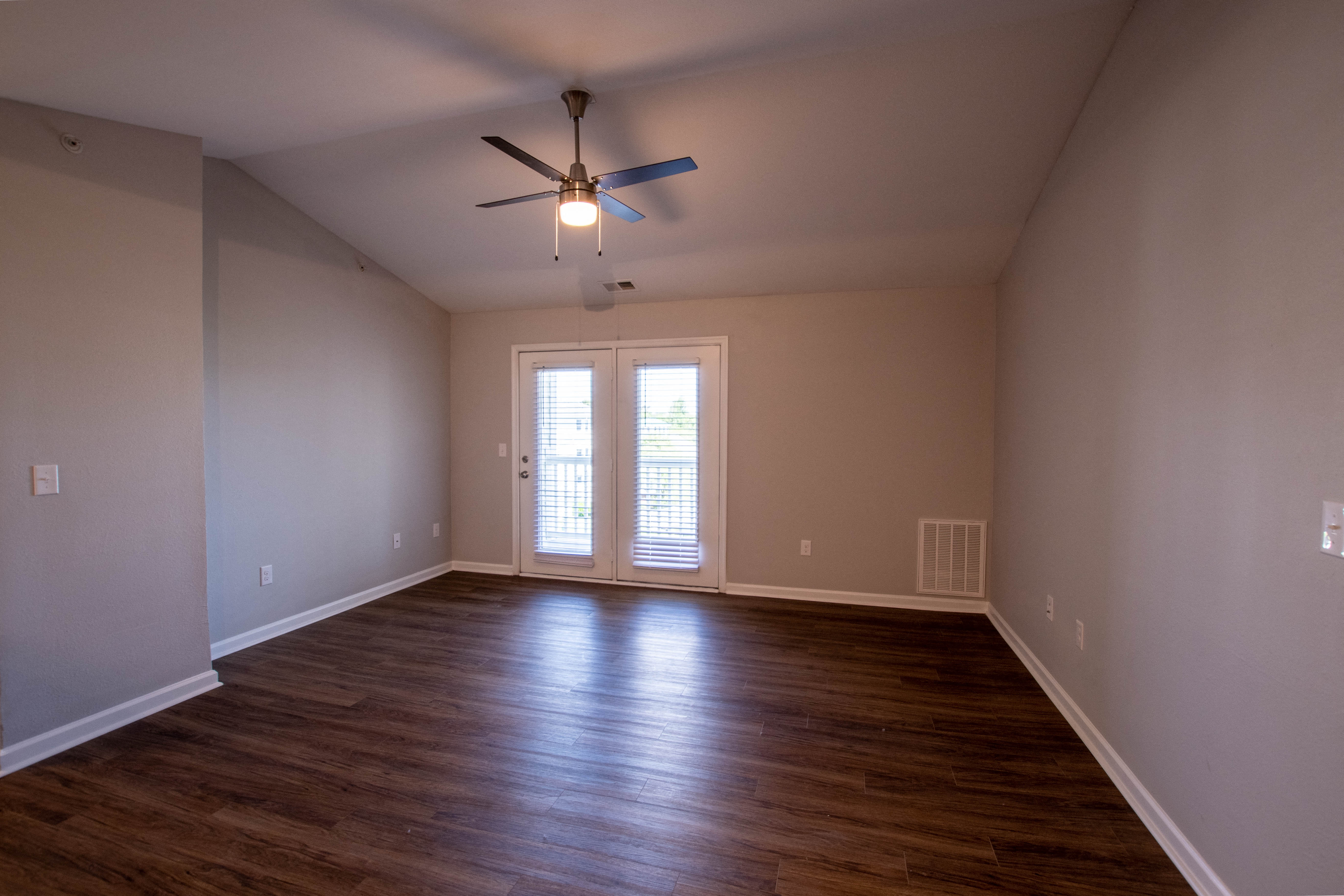 an empty living room with wooden floors and a ceiling fan