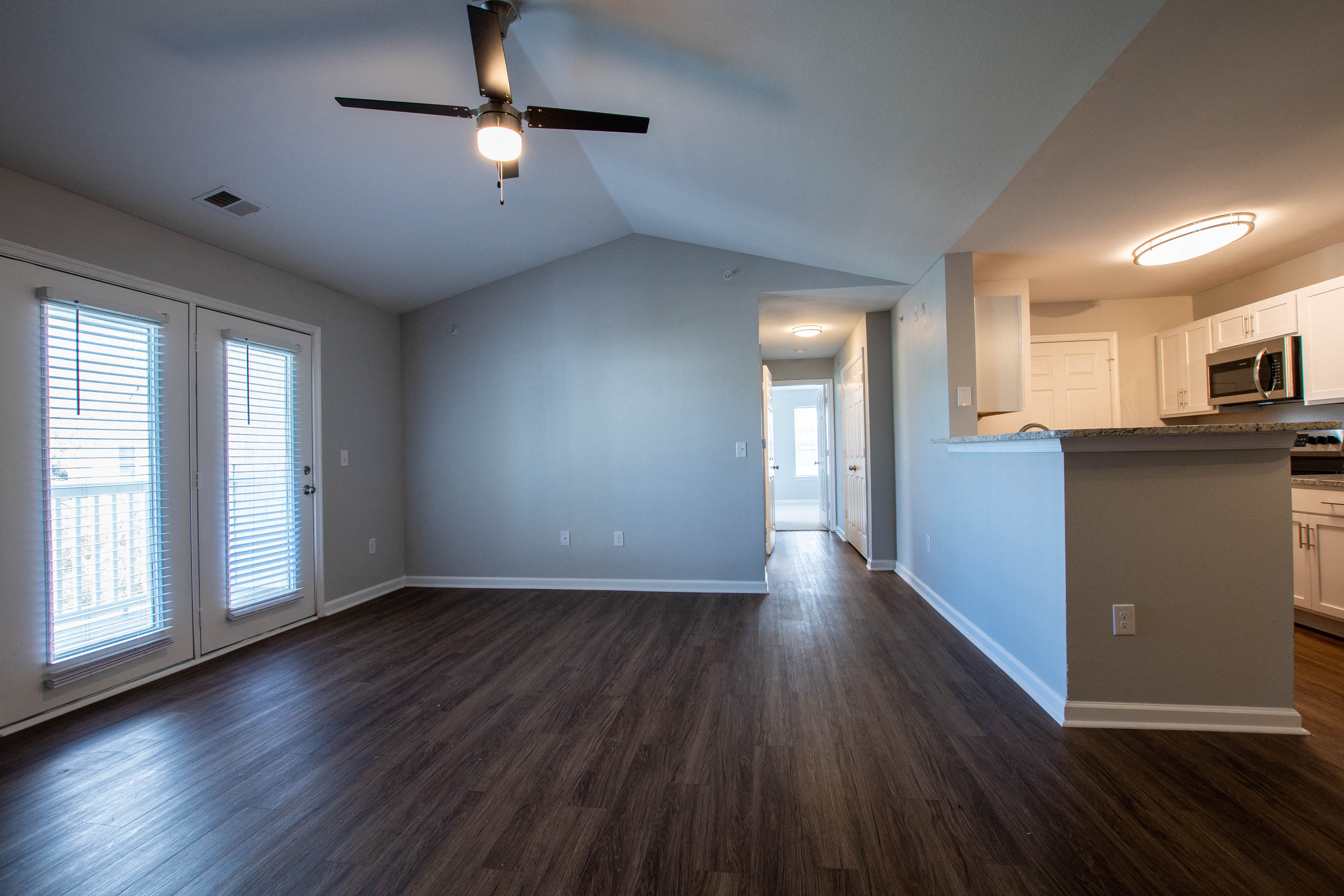 an empty living room and kitchen with wood floors and a ceiling fan