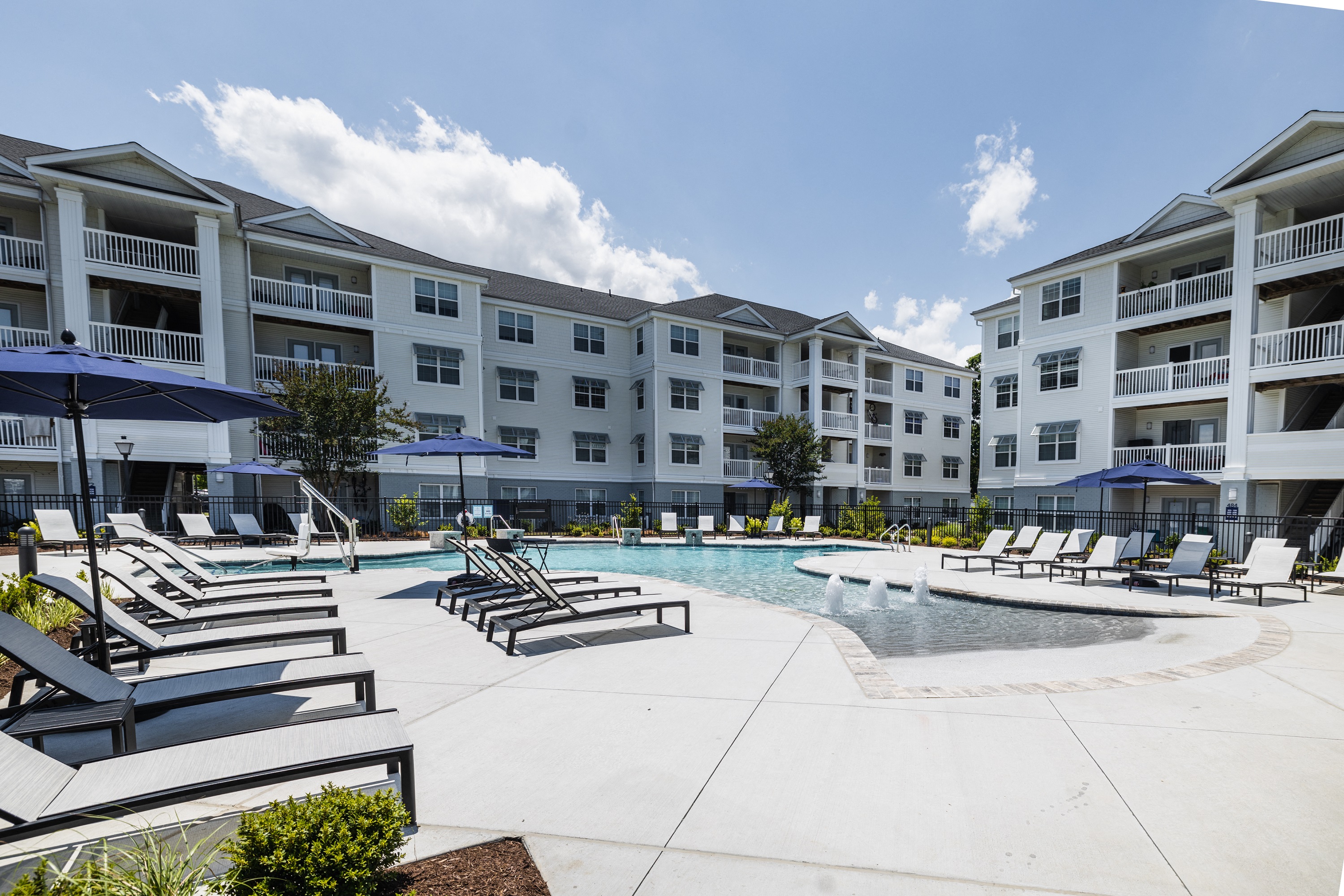 a pool with lounge chairs and umbrellas in front of an apartment building
